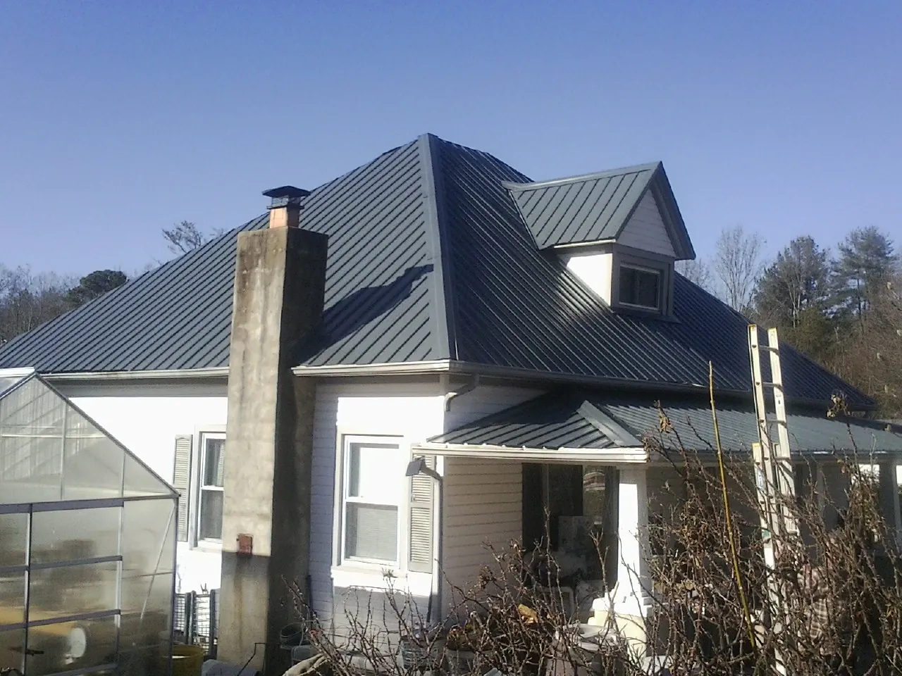 Dark blue standing seam metal roof on a white farmhouse with dormer — Slate & Tile Roof Repair by Roofing Brothers in Spring City