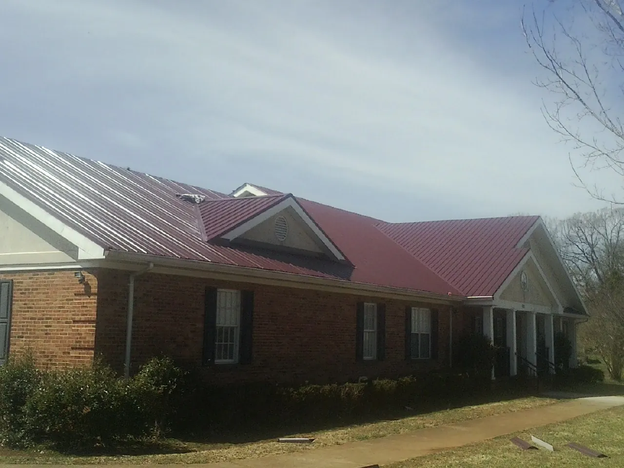 Red metal roof with gabled entries on a long brick building, from a Hail Damage Roof Repair job in Spring City