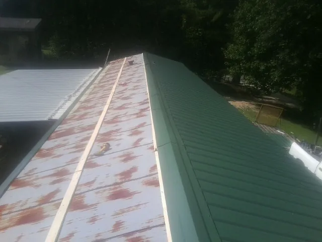 Old rusted panels beside newly installed green metal roofing — Wind Damage Roof Repair by Roofing Brothers in Spring City